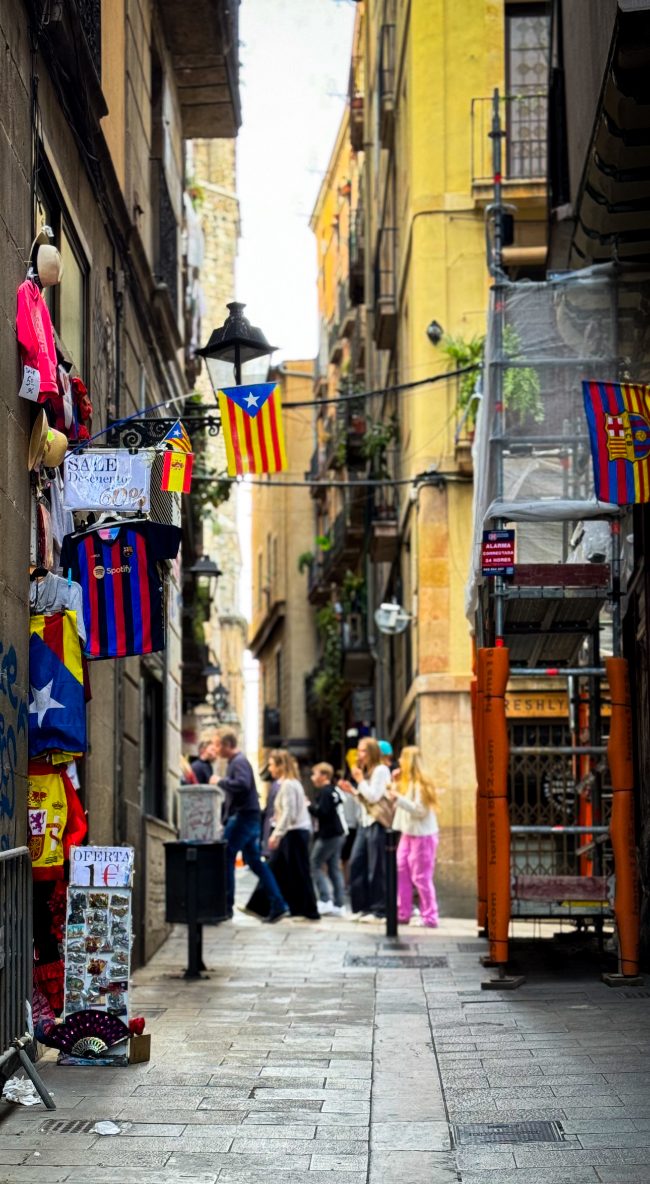 A busy alley in the Gothic Quarter with Catalan flags and local shopfronts
